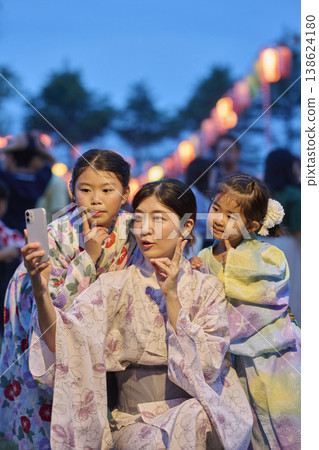 A mother and her two daughters, dressed in yukata, take a photo with their smartphone. A mother and her two daughters, dressed in yukata, take a photo with their smartphone. 138624180