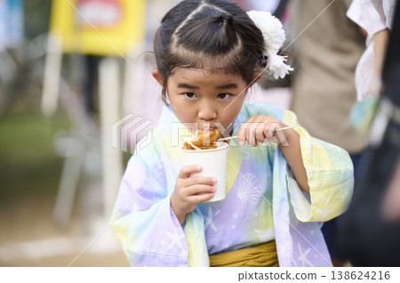 一個穿著浴衣的女孩在街上攤吃炸雞。 一個穿著浴衣的女孩在街上攤吃炸雞。 138624216
