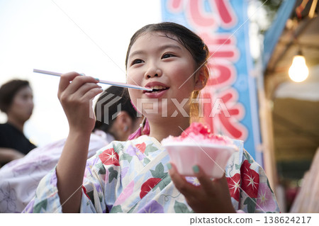 A smiling girl in a yukata eating shaved ice. A smiling girl in a yukata eating shaved ice. 138624217
