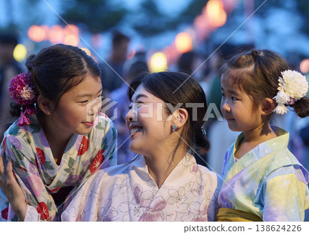 A mother and her daughters, both wearing yukata, are smiling and standing close together. A mother and her daughters, both wearing yukata, are smiling and standing close together. 138624226