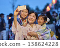 A family in yukata taking commemorative photos with their smartphone at a summer festival. 138624228