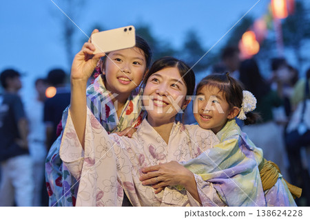A family in yukata taking commemorative photos with their smartphone at a summer festival. A family in yukata taking commemorative photos with their smartphone at a summer festival. 138624228