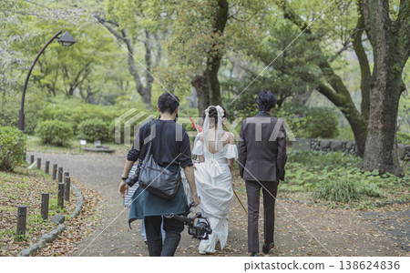 A woman in a wedding dress and staff heading to a park for a photoshoot. 138624836