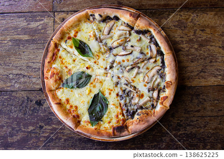 Freshly baked pizza on a wooden table pizza is generously topped with melted mozzarella cheese sauteed mushrooms and fresh basil leaves, served on a black ceramic plate. Top view. Freshly baked pizza on a wooden table pizza is generously topped with melted mozzarella cheese sauteed mushrooms and fresh basil leaves, served on a black ceramic plate. Top view. 138625225