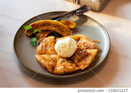 Banana roti topping with vanilla ice cream is arranged on a brown plate on the table. Select Focus. 138625227