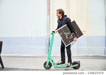 Man rides electric scooter while carrying solar panel. Integration of solar power as sustainable energy source for charging electric scooters, promoting eco-friendly urban transportation. Man rides electric scooter while carrying solar panel. Integration of solar power as sustainable energy source for charging electric scooters, promoting eco-friendly urban transportation. 138625479
