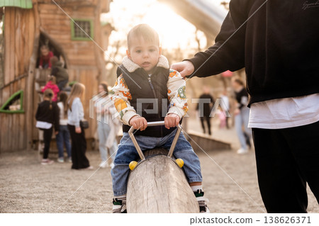 Father helping toddler balance on playground beam at sunset Father helping toddler balance on playground beam at sunset 138626371