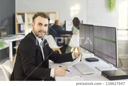 Smiling accountant at desk with spreadsheets on dual monitors in bright office Smiling accountant at desk with spreadsheets on dual monitors in bright office 138627847
