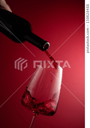 Pouring red wine from a bottle into a glass. 138628488