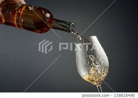 Pouring white wine from a bottle into a glass. 138628490