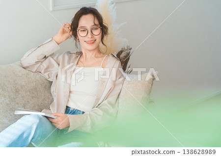 一位衣著時尚的亞洲女性坐在客廳的沙發上閱讀雜誌。 138628989