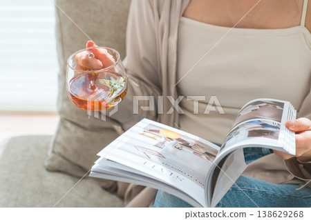 A stylish Asian woman sitting on the sofa in the living room and reading a magazine during tea time 138629268