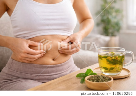 Woman touching belly with herbal tea for digestion and wellness concept 138630295