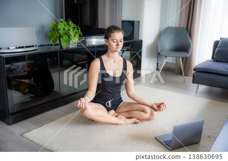 Young woman in sportswear doing yoga exercises on mat in living room. Online workout, fitness, practicing and meditation at home Young woman in sportswear doing yoga exercises on mat in living room. Online workout, fitness, practicing and meditation at home 138630695
