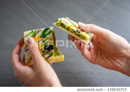Trend Dubai white chocolate with pistachio paste and kataifi dough in woman hands. Confectionery handmade sweets at home in the kitchen.  138630725