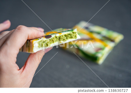 Piece of trend Dubai white chocolate with pistachio paste and kataifi dough in woman hand. Confectionery handmade sweets at home in the kitchen.  138630727