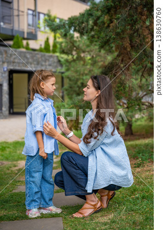 Mother and daughter wearing matching striped shirts and jeans while spending time together outdoors. Concept of family bonding, fashion harmony and casual everyday moments. Mother and daughter wearing matching striped shirts and jeans while spending time together outdoors. Concept of family bonding, fashion harmony and casual everyday moments. 138630760