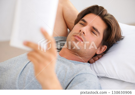 Man, bedroom and reading story in book, interesting novel and learning knowledge at home. Serious guy relax with notebook of fiction for break, studying literature or hobby to enjoy in comfort on bed 138630906