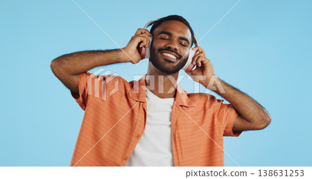 Black man, headphones and dancing to music with happiness and energy in studio on blue background. Techno, rave and fun with audio streaming, dancer is excited with smile and wireless technology Black man, headphones and dancing to music with happiness and energy in studio on blue background. Techno, rave and fun with audio streaming, dancer is excited with smile and wireless technology 138631253