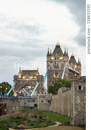 Golden illumination accents the bridge's Gothic tower and arch, set against a muted, wintry sky. The distinctive blue cables provide a vivid counterpoint to the historic stonework. In the foreground, Golden illumination accents the bridge's Gothic tower and arch, set against a muted, wintry sky. The distinctive blue cables provide a vivid counterpoint to the historic stonework. In the foreground, 138631595