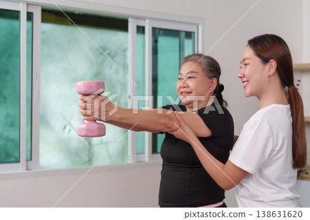 Senior woman lifting dumbbells with trainer's guidance 138631620