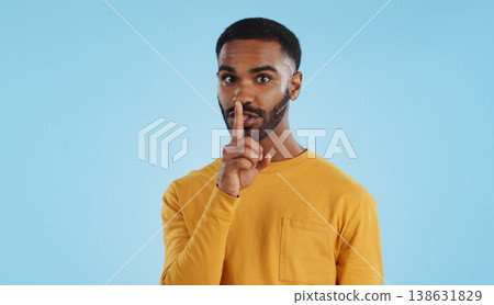Secret, face and man with finger on lips in studio for quiet, privacy or hush news on blue background. Whisper, drama and portrait of guy model with confidential hand emoji for gossip or announcement 138631829