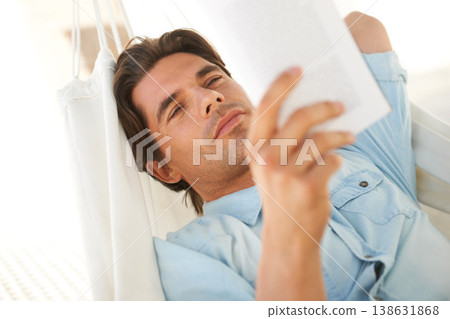 Reading, relaxing and young man on a hammock with a book for information or knowledge in backyard. Resting, calm and male person enjoying a story or novel on a body swing outdoor at modern apartment. 138631868