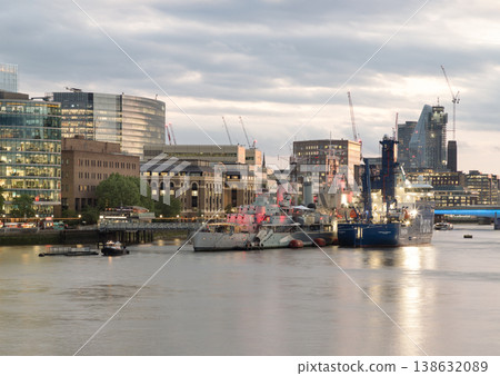 A wide-angle dusk shot of the London South Bank featuring HMS Belfast and adjacent shipping vessels. The image showcases the architectural contrast between historic naval landmarks and the modern City A wide-angle dusk shot of the London South Bank featuring HMS Belfast and adjacent shipping vessels. The image showcases the architectural contrast between historic naval landmarks and the modern City 138632089