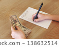 Kid hands holding dollar bills while writing finance calculations on paper, child learning budgeting and money skills, financial literacy education 138632514