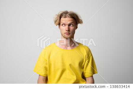 Young man with blond hair and a casual yellow t-shirt looking away with a suspicious and curious expression, communicating concepts of doubt, skepticism, and uncertainty Young man with blond hair and a casual yellow t-shirt looking away with a suspicious and curious expression, communicating concepts of doubt, skepticism, and uncertainty 138633414