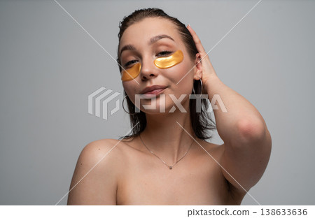 Young woman with radiant skin applying golden eye patches, treating her delicate under-eye area with a moisturizing cosmetic product for beauty and self-care Young woman with radiant skin applying golden eye patches, treating her delicate under-eye area with a moisturizing cosmetic product for beauty and self-care 138633636
