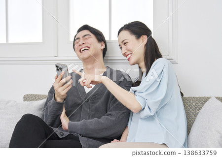 A couple talking while looking at their smartphones in the living room. A couple talking while looking at their smartphones in the living room. 138633759