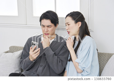A couple looking at their smartphones in the living room, troubled. A couple looking at their smartphones in the living room, troubled. 138633760