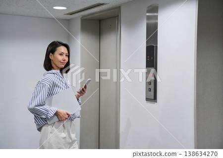 A businesswoman in an elevator lobby holding a laptop and a smartphone. A businesswoman in an elevator lobby holding a laptop and a smartphone. 138634270