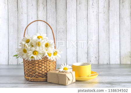 Happy birthday or mothers day concept; bouquet of white daisy flowers, craft gift box and yellow cup of tea on a wooden table; copy space Happy birthday or mothers day concept; bouquet of white daisy flowers, craft gift box and yellow cup of tea on a wooden table; copy space 138634502