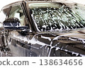 Car wash, close-up black car covered with thick foam on windshield and body at indoor station. Soap streaks and bubbles during cleaning process, glossy surface care, vehicle washing and detailing 138634656