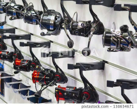 Different types of fishing reels displayed on a wall at a sporting goods store in bright lighting for customers to look at 138634671