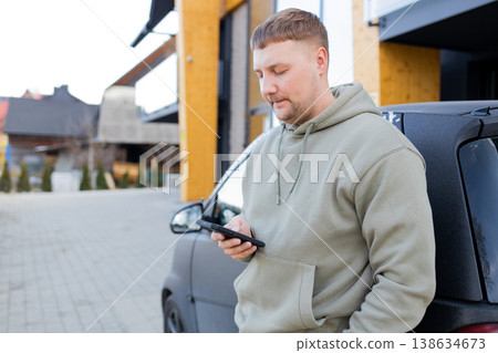 Man using smartphone standing near car outdoors 138634673