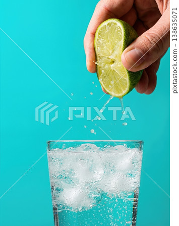 Hand Squeezing Lime Half with Flying Juice Droplets Isolated on a Solid Bright Turquoise Background Hand Squeezing Lime Half with Flying Juice Droplets Isolated on a Solid Bright Turquoise Background 138635071