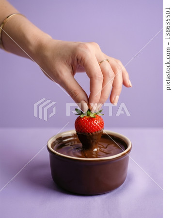 Hand Dipping Fresh Strawberry into Melted Glossy Chocolate Isolated on a Solid Soft Lavender Background 138635501