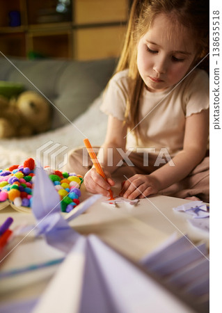 Little girl drawing on paper craft shapes with marker at table in home 138635518
