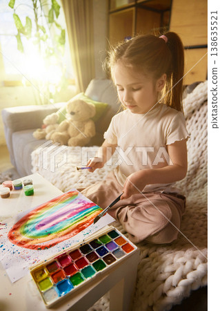 Little girl painting colorful rainbow with watercolor at table in cozy home. Little girl painting colorful rainbow with watercolor at table in cozy home. 138635521