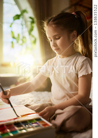 Close up little girl painting with watercolor palette in soft natural light. Concept of fine motor skills, sensory learning, attention focus and creative practice Close up little girl painting with watercolor palette in soft natural light. Concept of fine motor skills, sensory learning, attention focus and creative practice 138635522