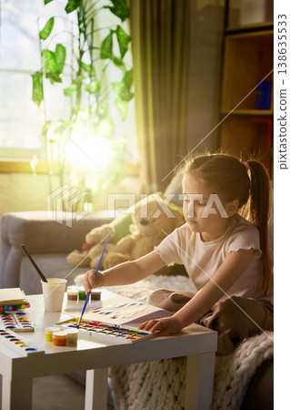 Young girl painting with watercolor set in warm sunlight at home interior. 138635533