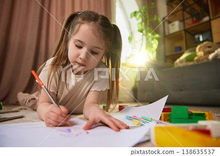 Little girl drawing on paper with warm sunlight flare in modern home interior. Little girl drawing on paper with warm sunlight flare in modern home interior. 138635537