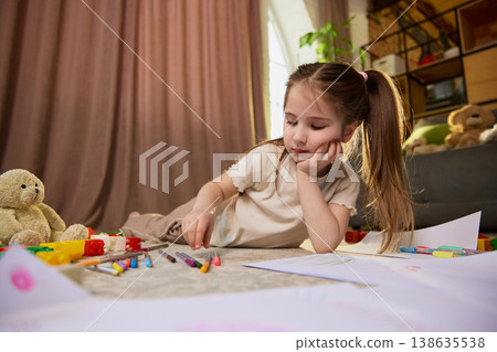 Young girl choosing colored pencils and drawing on paper in cozy living room. Young girl choosing colored pencils and drawing on paper in cozy living room. 138635538