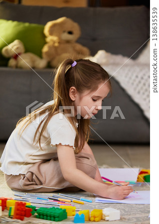 Little girl drawing with colored pencils sitting on floor near toys at home. Little girl drawing with colored pencils sitting on floor near toys at home. 138635539