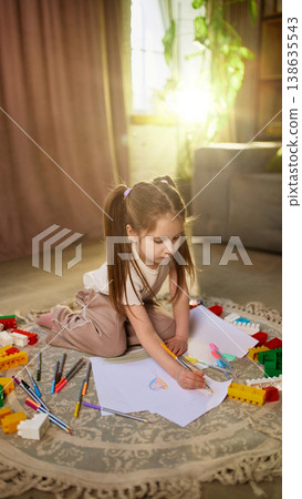 Young girl drawing with pencil sitting on rug in cozy home interior 138635543