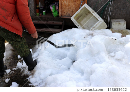 A gardener with a shovel stands by a snowdrift next to a shed in a spring garden 138635622