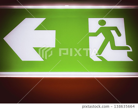 Green emergency exit sign with running figure and arrow direction, symbolizing safety guidance, evacuation route, fire escape, building regulation, and emergency preparedness concept Green emergency exit sign with running figure and arrow direction, symbolizing safety guidance, evacuation route, fire escape, building regulation, and emergency preparedness concept 138635664